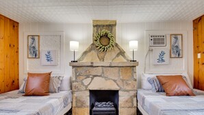 Une chambre avec deux lits, une cheminée en pierre et des œuvres d’art encadrées accrochées aux murs.