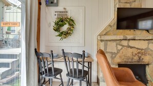 L’intérieur chaleureux d’un chalet avec une cheminée en pierre, un téléviseur fixé au-dessus et un coin repas comprenant deux chaises et une table.