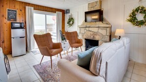 Un salon chaleureux avec une cheminée en pierre, deux fauteuils en cuir, un canapé, un téléviseur et un four à micro-ondes.