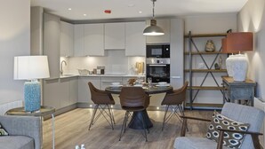 A modern kitchen with white cabinets, a dining table with four chairs, and a hanging pendant light. - 5* Luxury, City Centre, Brand New Development (Belfast)