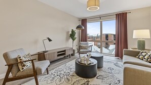A modern living room with a sofa, armchair, coffee table, and a large window with curtains. - 5* Luxury, City Centre, Brand New Development (Belfast)