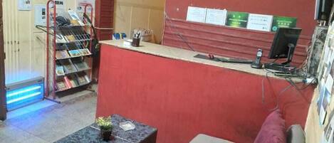 A reception area with a red counter, clocks displaying different time zones, a small table with a plant, and a seating area with a couch.