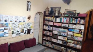 Una sala acogedora con un sofá, una estantería y una pared decorada con fotos y notas.
