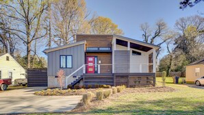 Een modern gelijkvloers huis met een rode deur, een overdekte veranda en een kleine voortuin met beplanting.