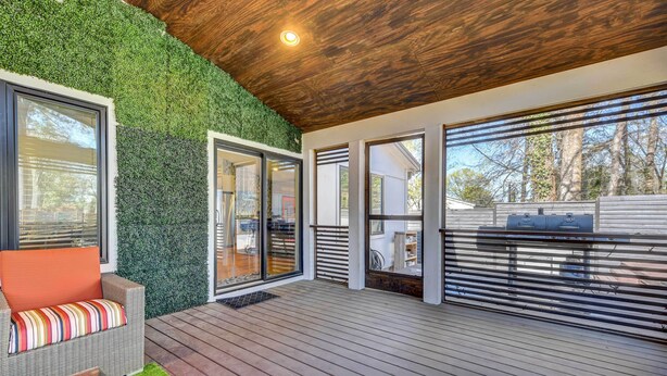 Een modern terras buiten, met een houten vloer, een groene wand en een glazen deur naar een terras.