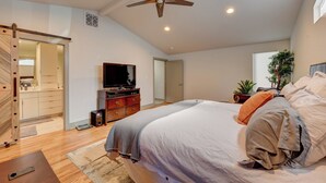 Een slaapkamer met een bed, plafondventilator, televisie, dressoir en een deur naar een andere kamer.