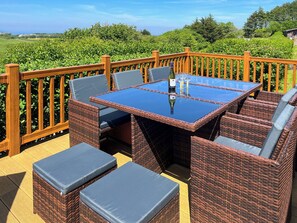 A wicker outdoor seating area with a glass table, cushioned chairs, and a wooden deck railing.