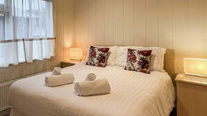 Une chambre d’hôtel avec un grand lit, deux tables de chevet avec des lampes et une fenêtre avec des rideaux légers.