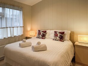 A hotel room with a large bed, two bedside tables with lamps, and a window with sheer curtains.
