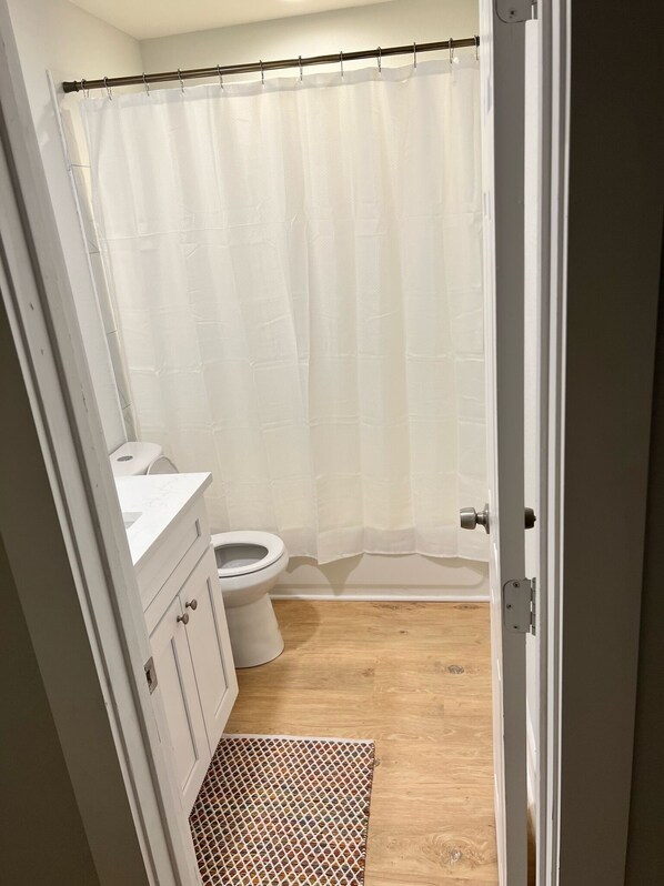 A small bathroom with a toilet, a sink, and a shower curtain. - Home Away 2BR (Wylie)