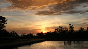A sunset over a body of water with silhouettes of trees and a bench. - Lodge Ylang Ylang (Cóbano)