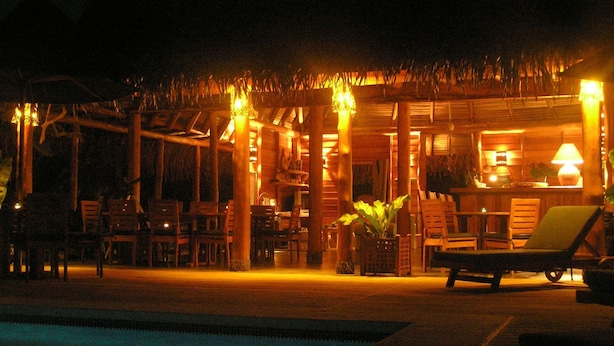 A nighttime view of a resort with a pool, lounge chairs, and a thatched-roof structure with tables and chairs. - Lodge Ylang Ylang (Cóbano)