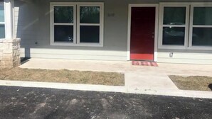 Una casa a un piano con una porta rossa, due finestre e un piccolo giardino.