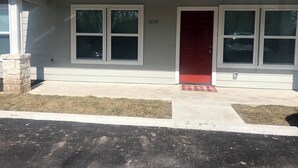 A single-story house with a red door, two windows on the front, and a stone pillar. - Elegant 2 Bedroom Apartment Home (Wylie)