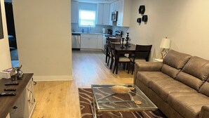 A living room with a brown leather sofa, a glass coffee table with decorative items, a wooden sideboard with remote controls, and a patterned rug. - Elegant 2 Bedroom Apartment Home (Wylie)