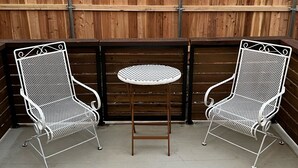 A patio area with two white metal chairs and a round table, enclosed by a wooden fence. - Elegant 2 Bedroom Apartment Home (Wylie)