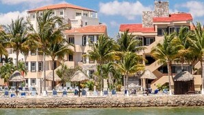 A beachfront hotel with multiple buildings, palm trees, and a clear blue sky.