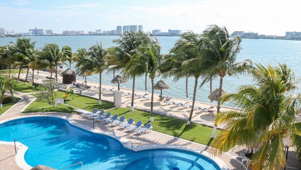 A swimming pool with lounge chairs and palm trees, overlooking a body of water and a city skyline.