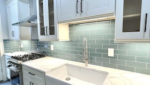 A modern kitchen with white cabinets, a stainless steel stove, and a tiled backsplash. - Private Vacation Resort:  Pool,  Spa, Gym, Kitchen, Laundry, in Tranquil Setting (Sugar Hill)