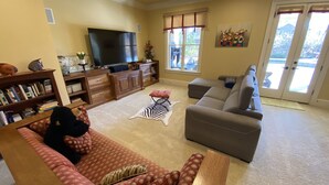 A living room with a sofa, a television, a bookshelf, and a window with a view. - Private Vacation Resort:  Pool,  Spa, Gym, Kitchen, Laundry, in Tranquil Setting (Sugar Hill)