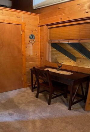 Um interior de madeira com uma mesa de jantar e cadeiras, uma janela com persianas, e uma porta de madeira.
