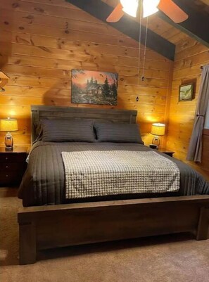 Quarto de cabana de madeira com uma cama, duas luminárias de cabeceira, um quadro na parede e um ventilador de teto.