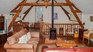 Uma sala de estar rústica com teto de madeira alto, sofás de couro, uma mesa de centro de madeira e uma escada que leva a um andar superior.