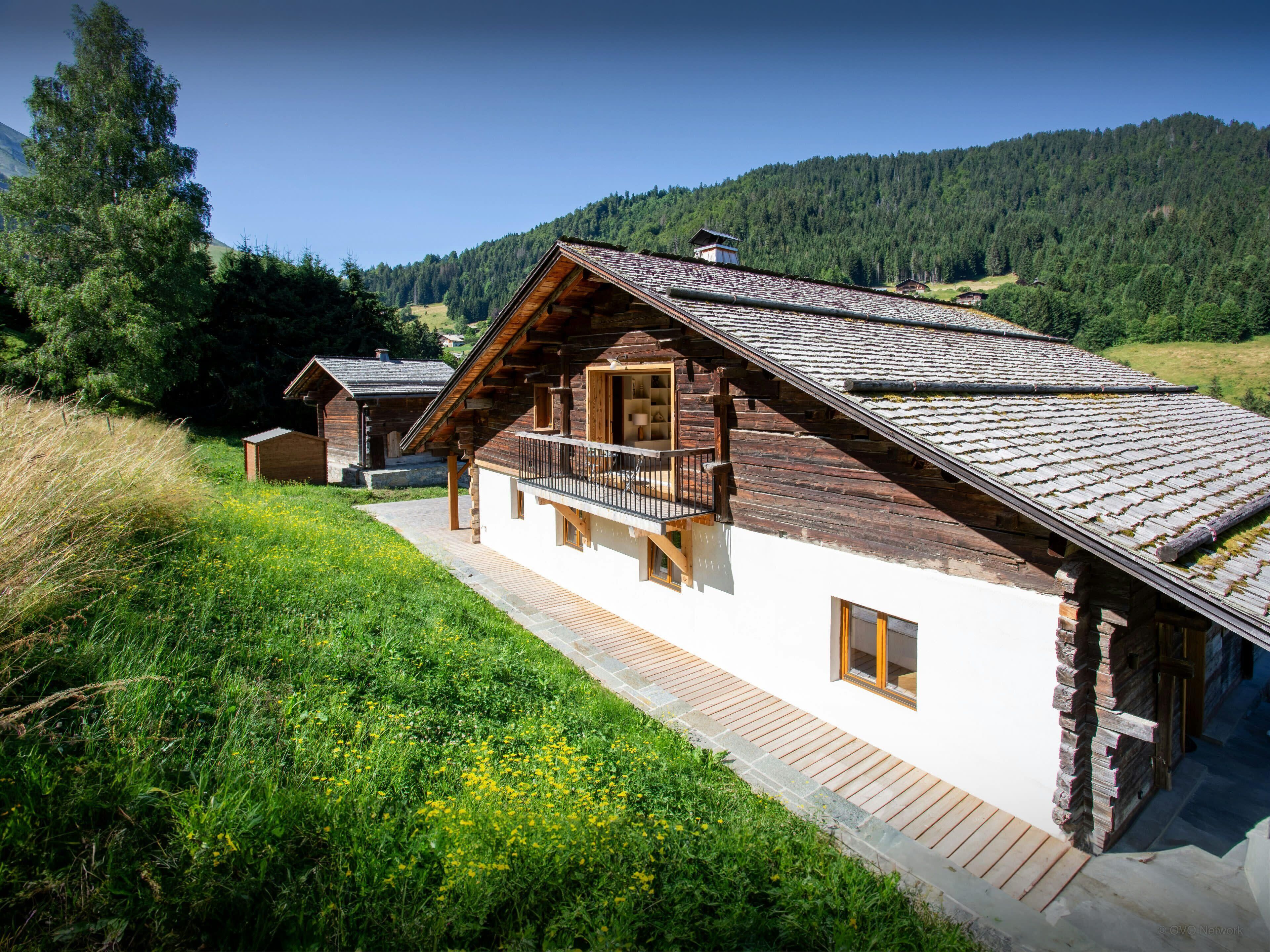Een houten chalet met balkon, gelegen in een bergachtig gebied met weelderige begroeiing.