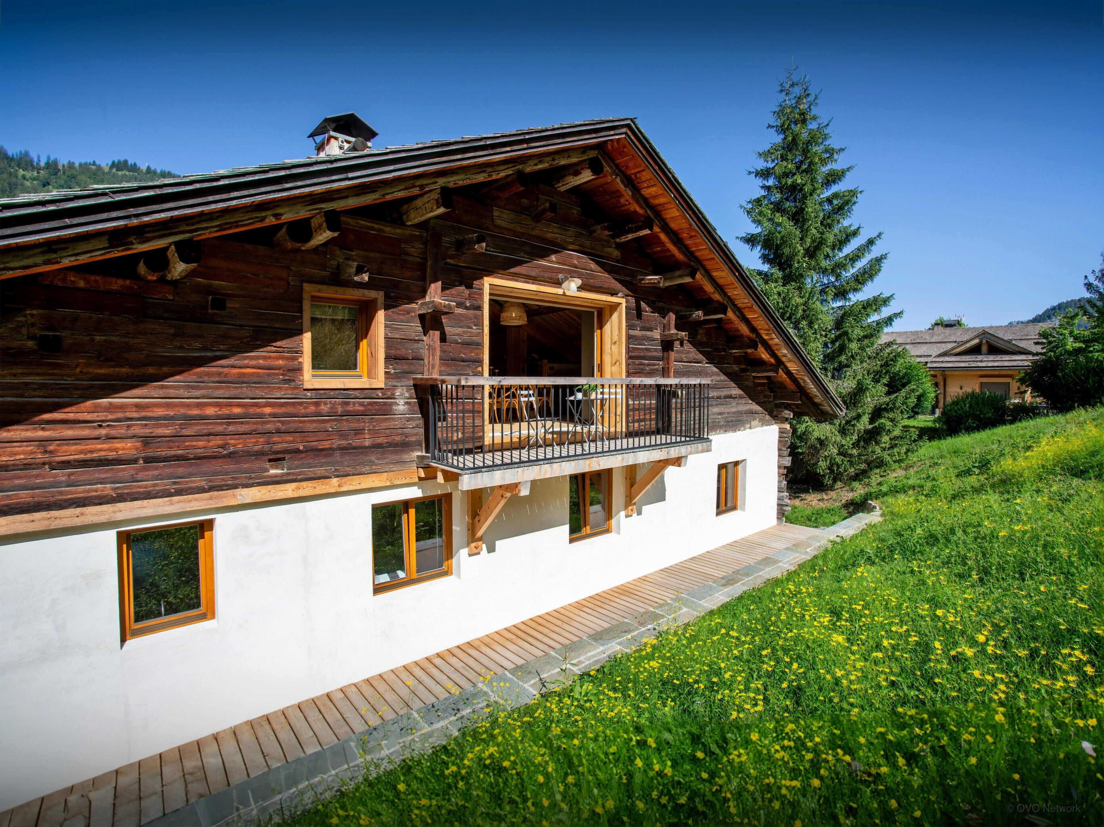 Eine Holzchalet mit Balkon, weißen Wänden und einem Steinweg, der zum Eingang führt.