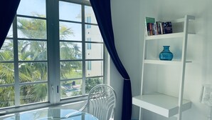 A room with a glass table, white chairs, a blue vase, and a white bookshelf with books and a decorative item. - CHARMING BRIGHT Ocean front - view  jacuzzi oven SoBe (Miami Beach)