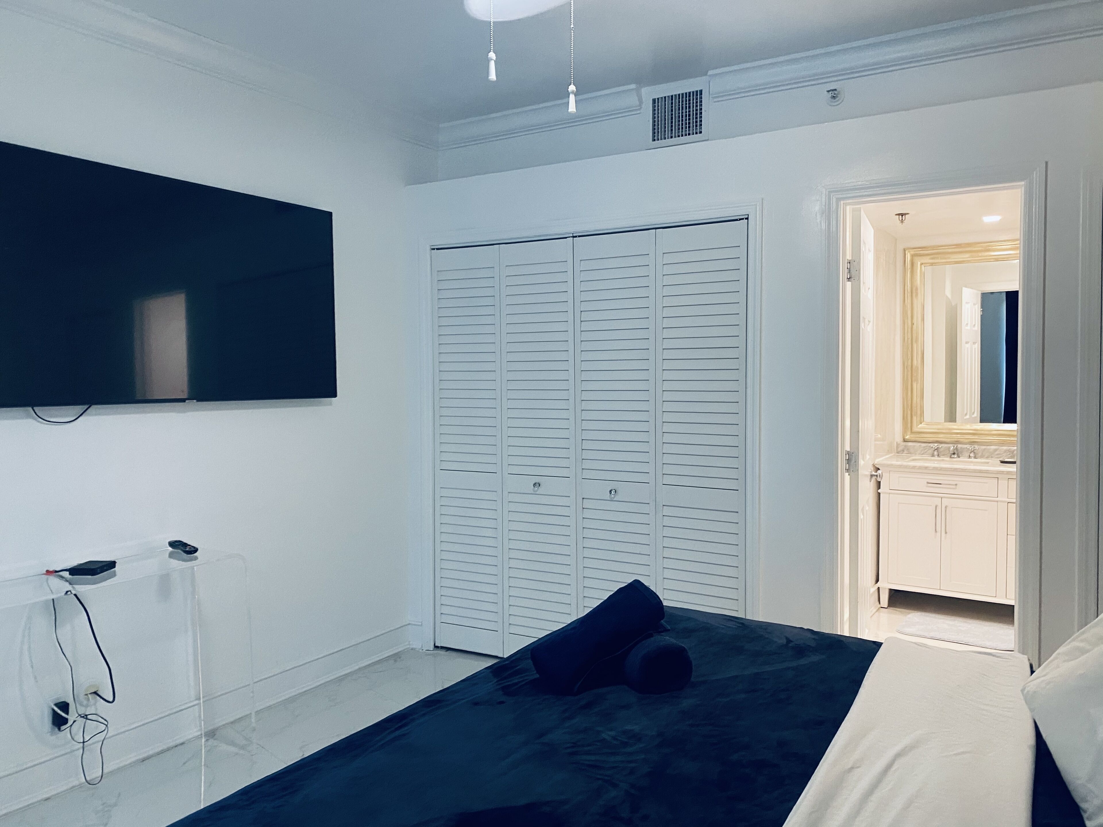 A bedroom with a bed, a TV mounted on the wall, a closet, and a bathroom visible through an open door.