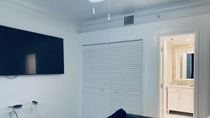 A bedroom with a bed, a TV mounted on the wall, a closet, and a bathroom visible through an open door. - CHARMING BRIGHT Ocean front - view  jacuzzi oven SoBe (Miami Beach)