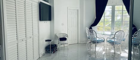 Een kamer met een witte plafondventilator, een aan de muur bevestigde televisie, een witte deur en een tafel met stoelen.