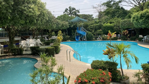 A swimming pool with a slide, surrounded by greenery and white plastic chairs. - Hotel El Broche (Yopal)