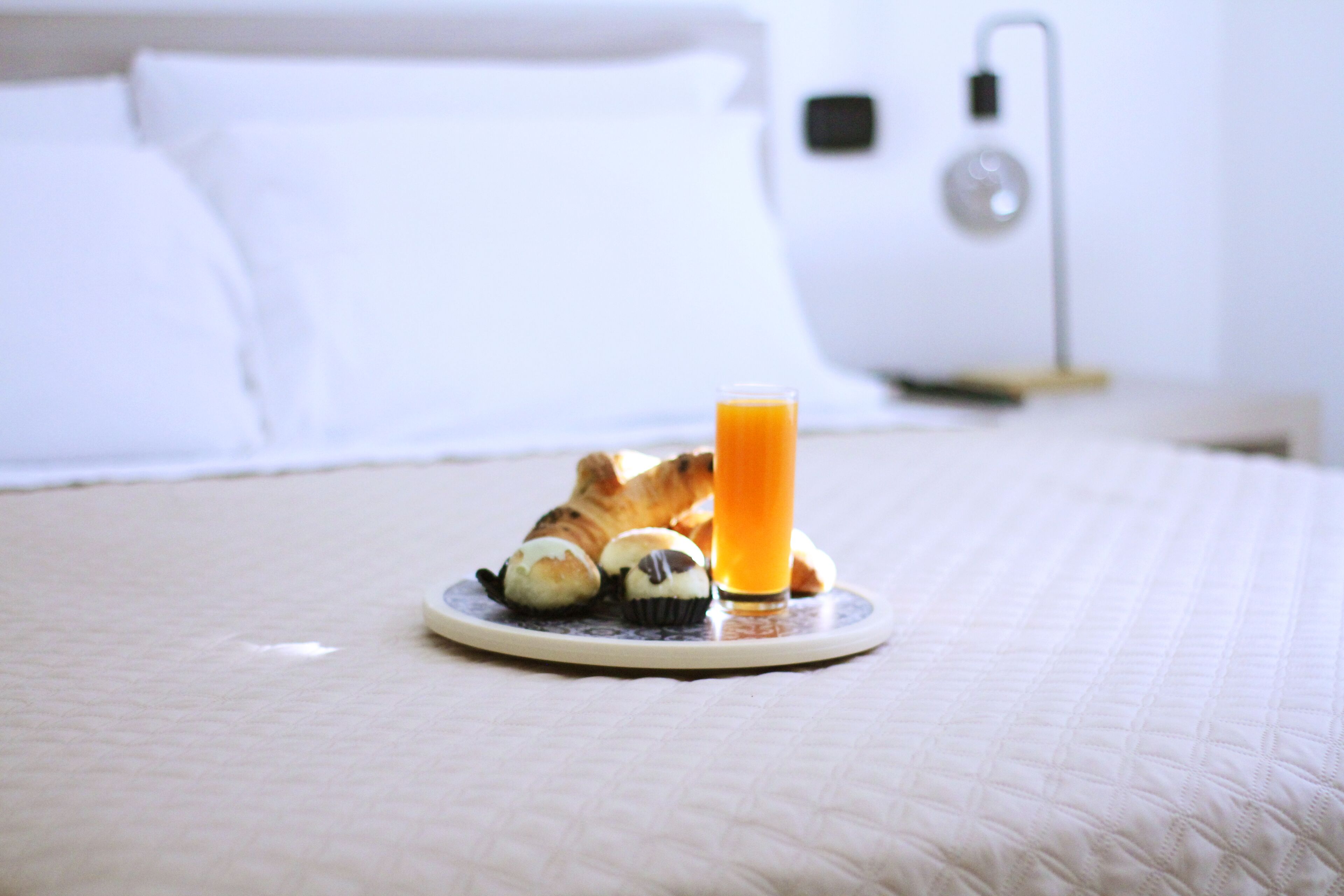 Un plateau de petit-déjeuner avec des croissants et un verre de jus d’orange, posé sur un lit recouvert d’une couverture blanche.