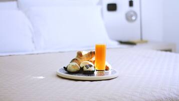 Un plateau de petit-déjeuner avec des croissants et un verre de jus d’orange, posé sur un lit recouvert d’une couverture blanche.