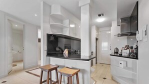 Een moderne keuken met witte kasten, een zwart aanrecht en twee houten krukken.