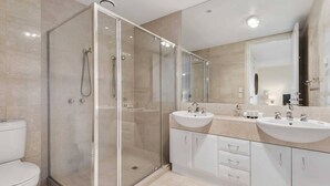 Een moderne badkamer met een douchecabine van glas, twee wastafels en een grote spiegel.