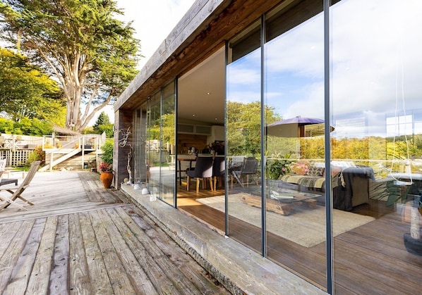 A modern house with a wooden deck, large glass windows, and a dining area with outdoor furniture.