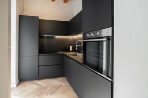 Een moderne keuken met donkere kastjes, een roestvrijstalen oven en een visgraat houten vloer.