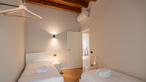 Ein Schlafzimmer mit zwei Betten, einer Holzbalkendecke, einer weißen Wand und einer Tür zu einem Badezimmer.
