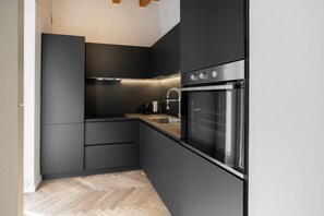 Une cuisine moderne avec des meubles de couleur sombre, un four en acier inoxydable et un parquet en bois disposé en chevrons.