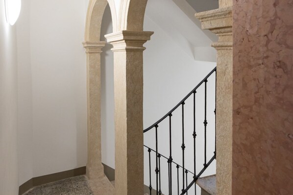 Un escalier avec une rampe en métal noir, des colonnes de couleur beige et des murs blancs.