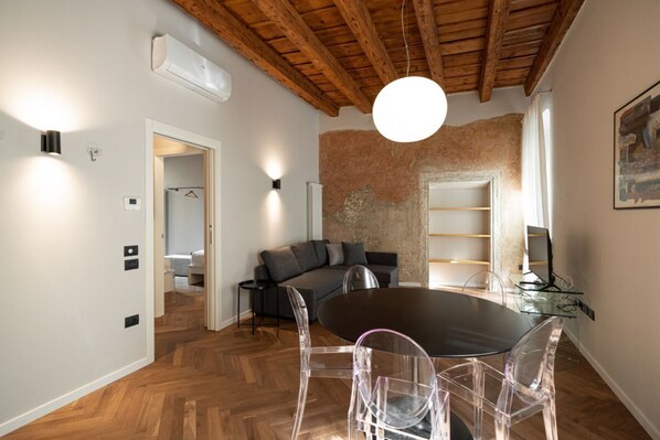 A modern living room with a wooden ceiling, a round dining table with clear chairs, a grey sofa, and a glass desk with a computer. - Elegant Frescoed Residence 200 meters from the Arena (Verona)