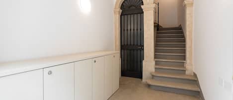 A hallway with a staircase leading to a dark door, white walls, and a light fixture above the door.