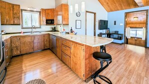 A spacious kitchen with wooden cabinets, a large island, and a high ceiling with exposed beams. - Le 277 - ZeNature /Lac Navigable (pets welcome) (Lac-Saint-Paul)