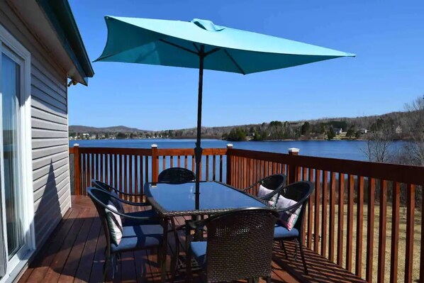 A deck with a table and chairs, a blue umbrella, and a view of a lake.