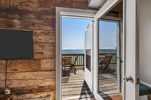 A wooden deck with a view of the ocean, a door leading to the deck, and a mounted TV. - Waterfront 1BR / Bayfront Deck / Beach access / Beach deck (Provincetown)