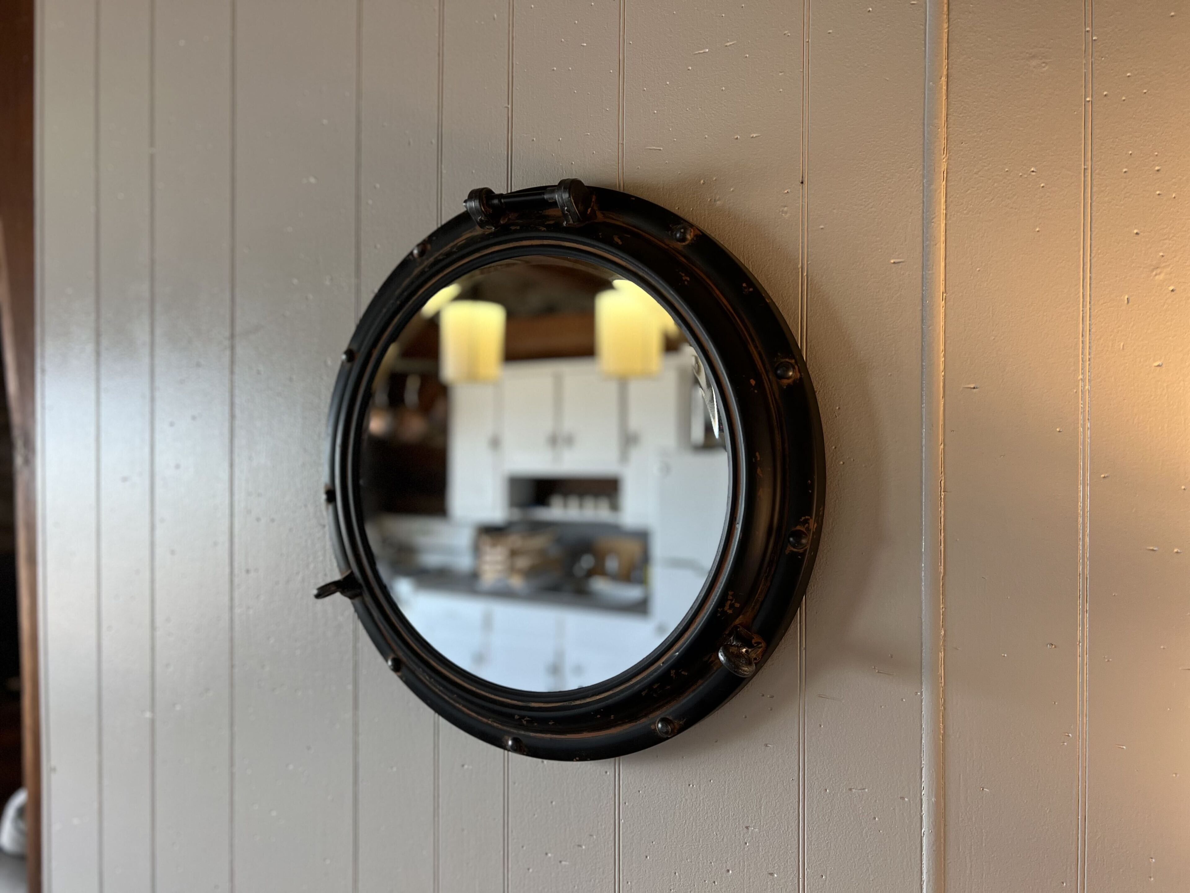 Un miroir rond, doté d’un cadre noir, est fixé sur un mur de couleur claire.