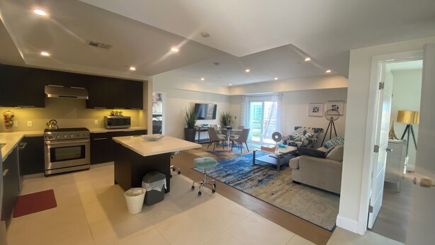 A modern kitchen with a central island, a dining area with a TV, and a living room with a sofa and a floor lamp. - Private Cozy Spacious Condo Unit with Gym— Walk distance to market (Los Angeles)